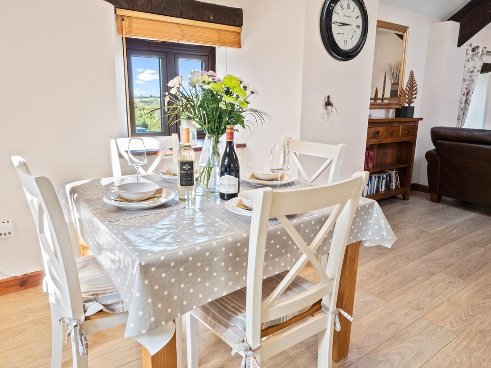 A photo of the dining table with wine bottles and flowers at The Hayloft at Tremaddock Farm Holiday Cottages