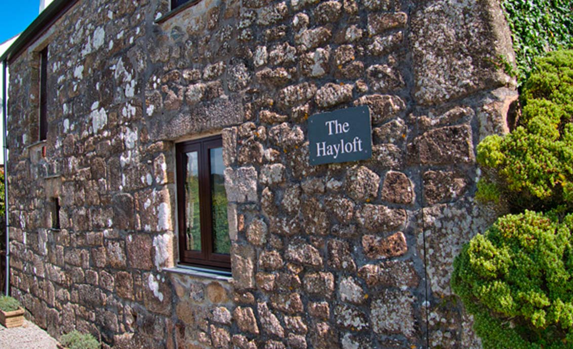 A photo of a slate sign on the outside of a stone house that reads "The Hayloft"