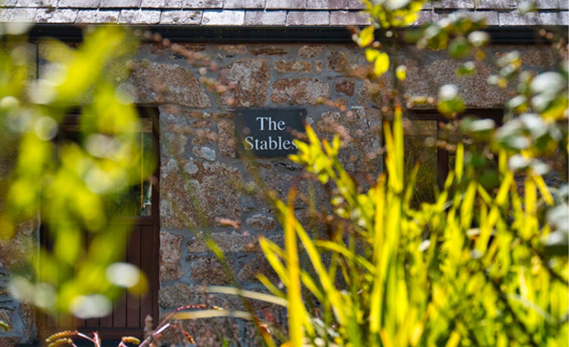 A photo of a slate sign on the outside of a stone house that reads "The Stables"